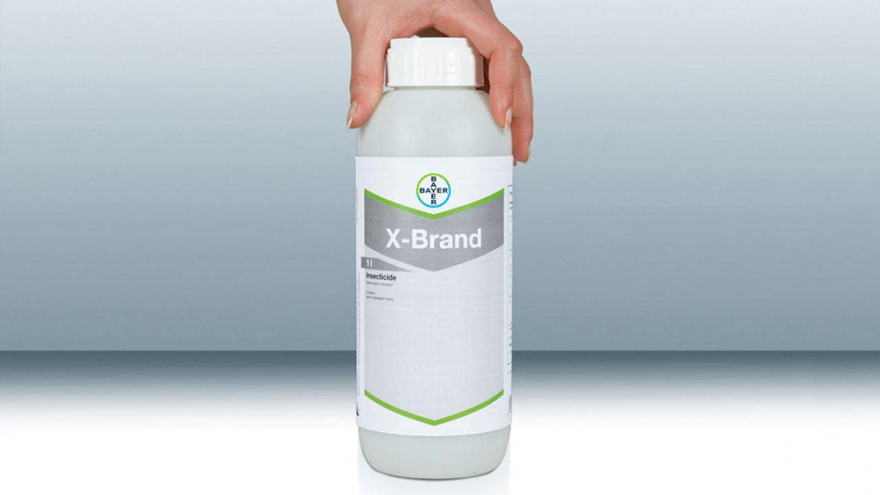 A hand holding a bottle labeled "X-Brand Herbicide.