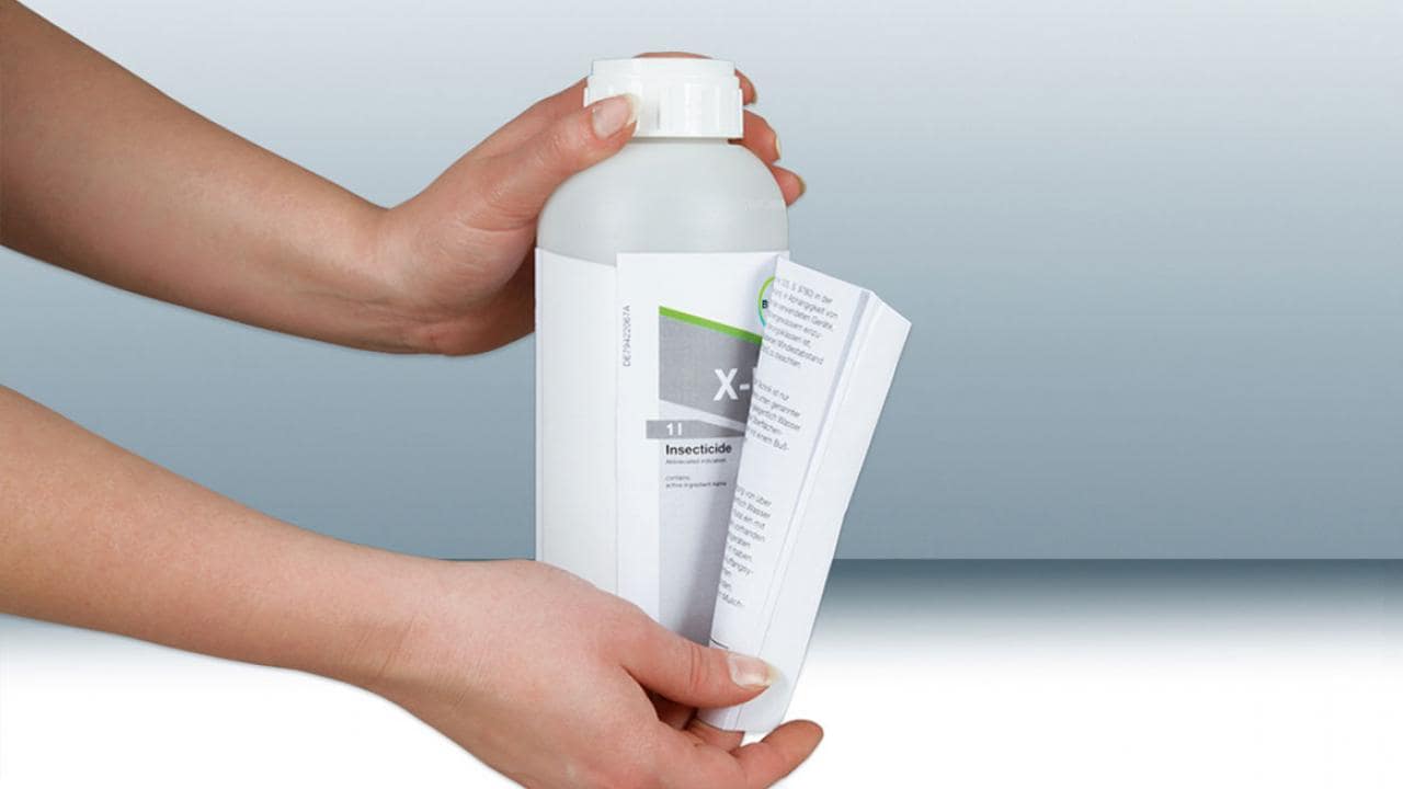 Hands holding a white bottle labeled as insecticide with a folded instruction leaflet attached.