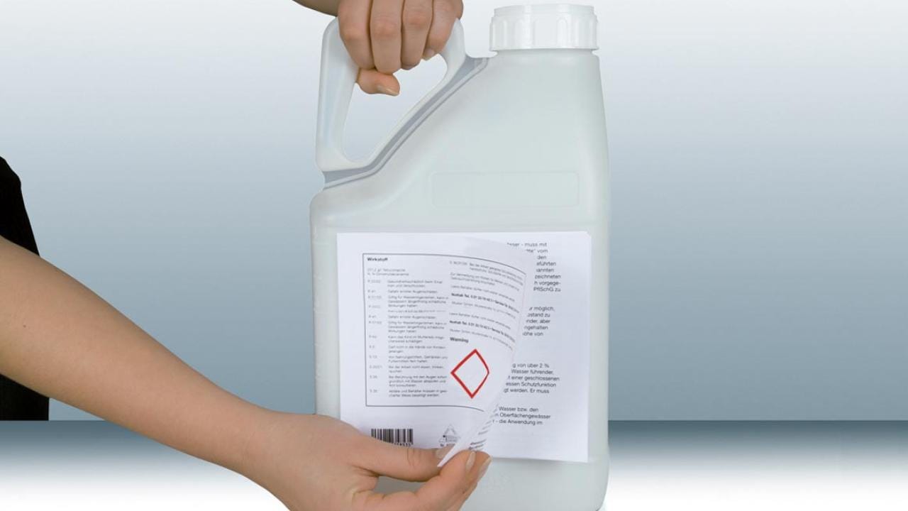 Person peeling a label from a large, white plastic container with a handle.