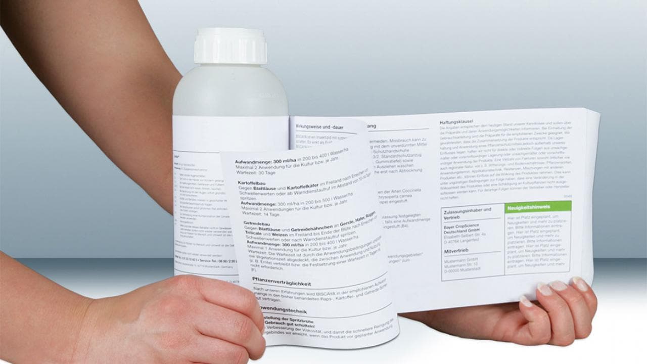 Hands open a large, unfolded label attached to a white bottle, revealing detailed text and information printed on the inside.