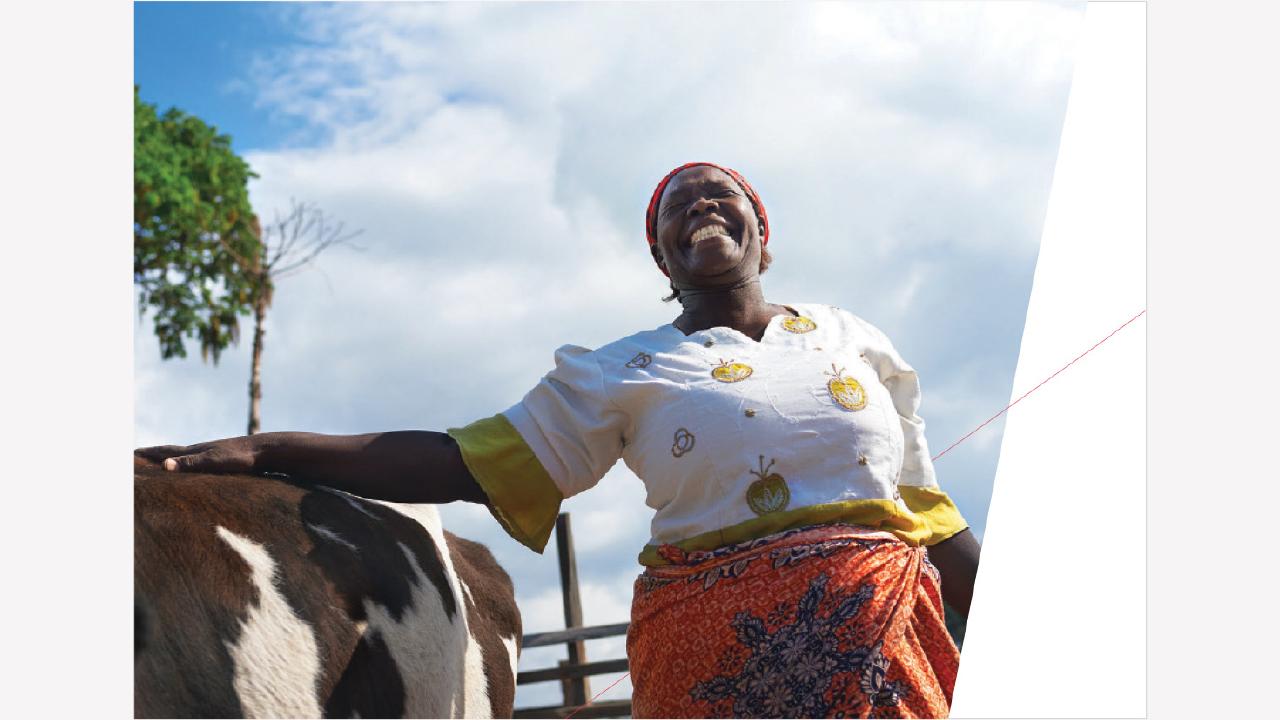 A woman is smiling while standing beside a cow outdoors, with a partly cloudy sky in the background.