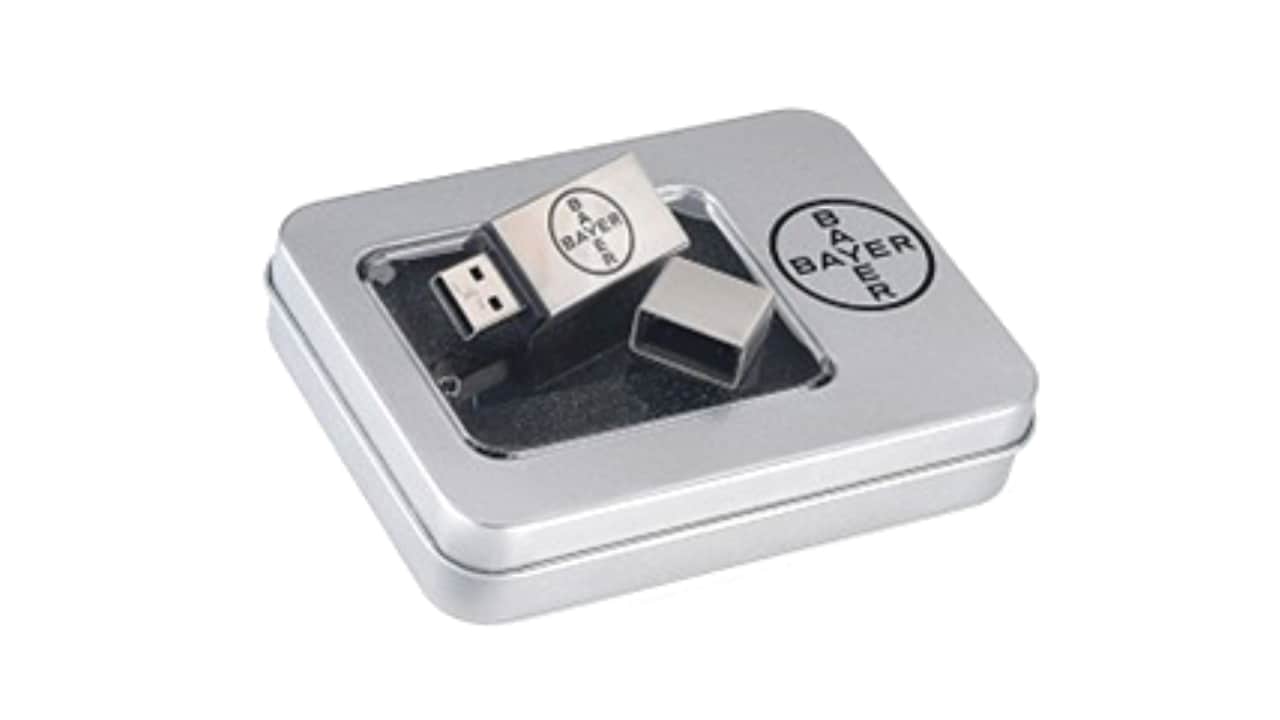 A metal USB drive with the Bayer logo is placed in a matching silver tin box with a clear lid.