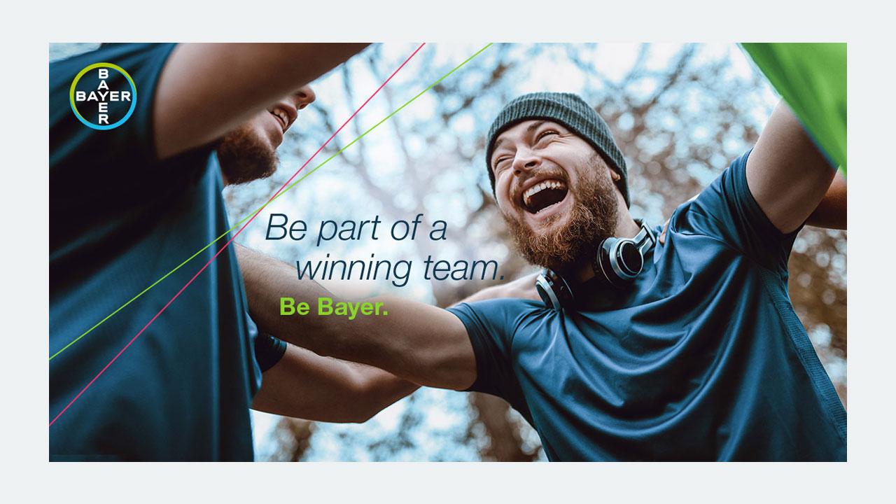 Two people in athletic clothing celebrate outdoors, surrounded by trees and a Bayer logo in the corner. The text reads, "Be part of a winning team. Be Bayer.