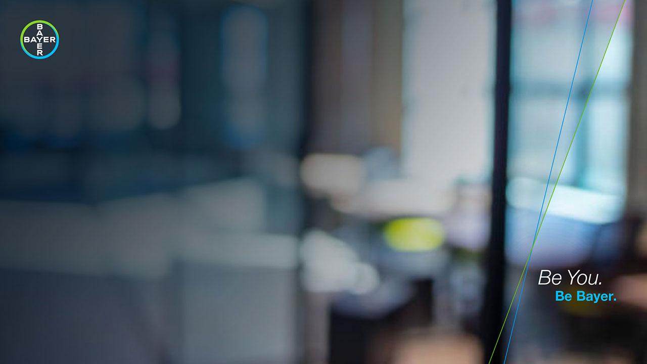 Blurred office setting with Bayer logo in the top left corner. Text on the right reads, "Be You. Be Bayer.