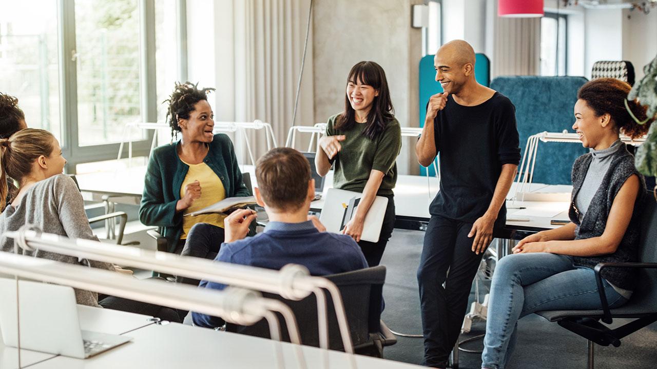 A diverse group of people sitting and standing in an office, engaged in a lively discussion.
