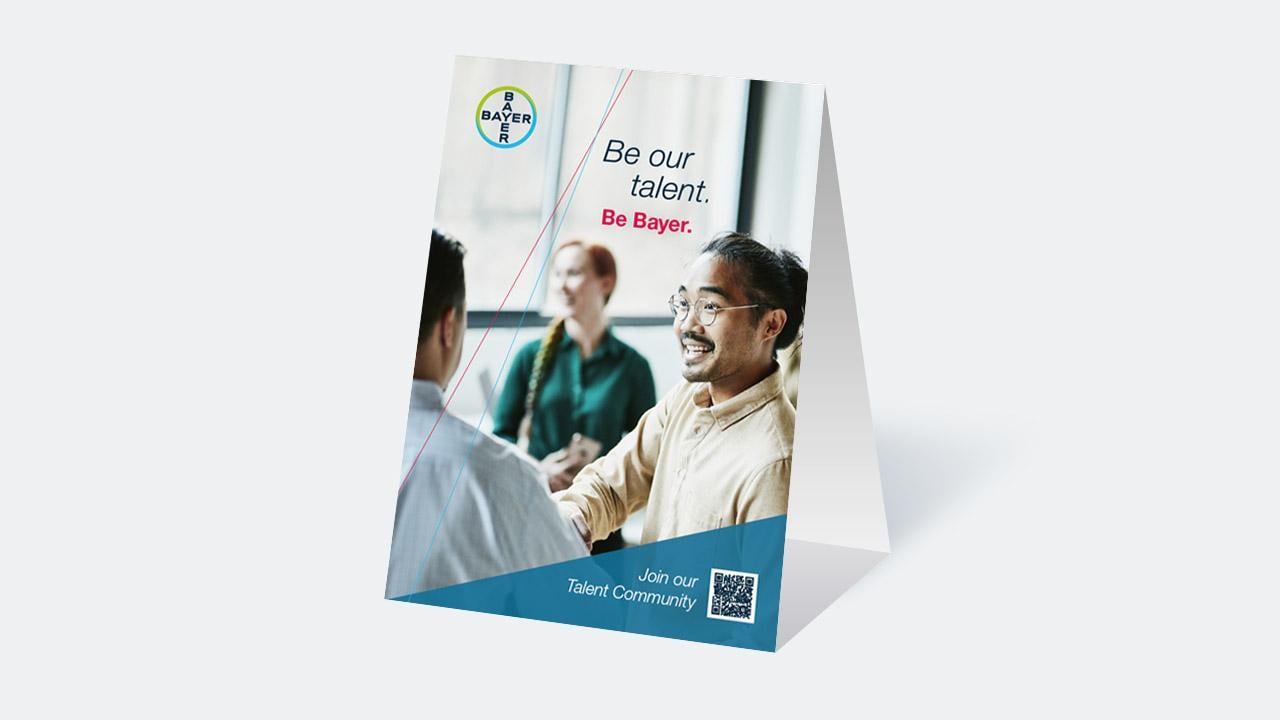 A Bayer recruitment poster shows a man shaking hands, with the text "Be our talent. Be Bayer." and a QR code below encouraging people to join their Talent Community.