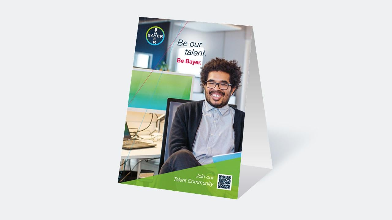 Recruitment poster featuring a smiling individual in an office, promoting Bayer with a QR code for joining their talent community.