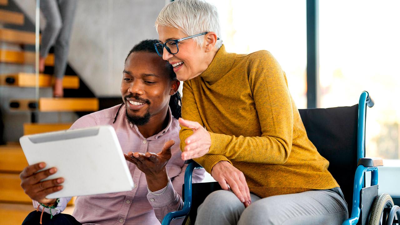 Man and woman in a wheelchair look at a tablet