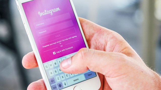 A hand holding a smartphone displaying the Instagram login screen with username and password fields.