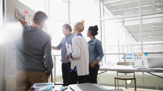 Four people collaborating and discussing in front of a whiteboard in a bright office setting.