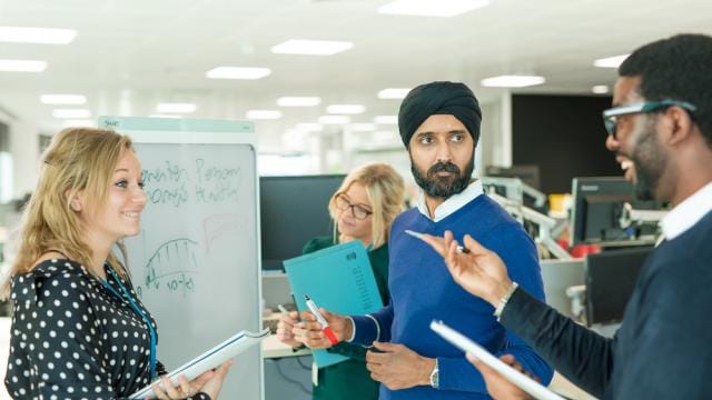 Four colleagues discussing in an office near a whiteboard with a chart.