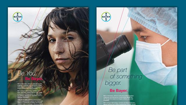 Two posters: one with a woman outdoors and text "Be You. Be Bayer," the other with a person in medical attire using a microscope and text "Be part of something bigger. Be Bayer.