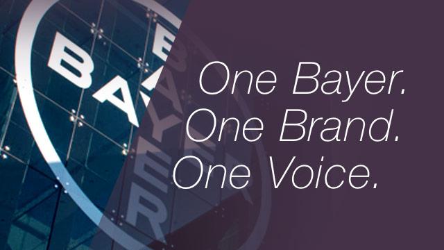 Glass building with Bayer logo on the left and the text "One Bayer. One Brand. One Voice." on the right against a dark background.