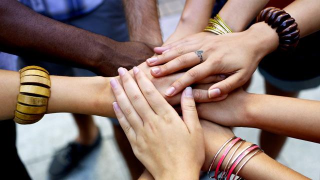 A group of diverse hands joined together in a stack, featuring various skin tones and bracelets.