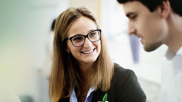 A woman wearing glasses smiles at a man during a conversation.