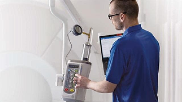 A person in a blue shirt operates medical imaging equipment in a hospital or clinical setting.