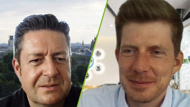 Two men in a split-screen video call. One is in front of a cityscape, the other in front of indoor decor. Both are smiling slightly.