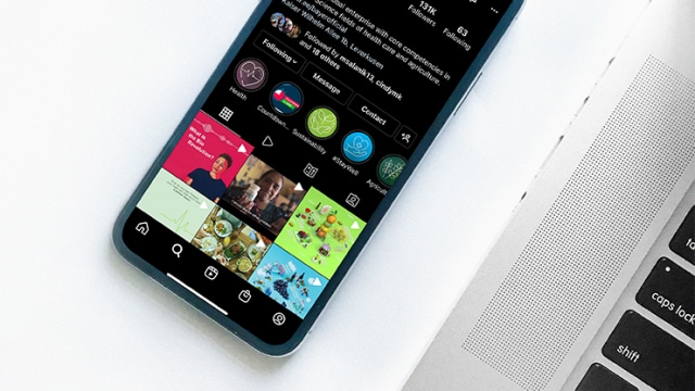 Smartphone displaying a social media app interface with a grid of photos next to a laptop on a white surface.