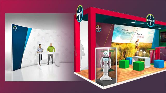 An exhibition booth with a Bayer logo, featuring a display stand, a robot, seating cubes, and a backdrop with fields and slogans. Two people stand at a reception counter.