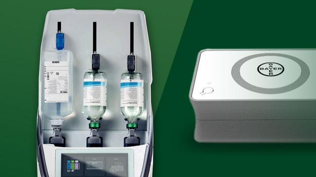 Medical infusion device with three fluid bags and control panel on the left; white rectangular device with a circular logo on the top right.