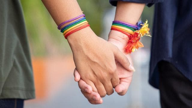 two hands holding hands with rainbow bracelets