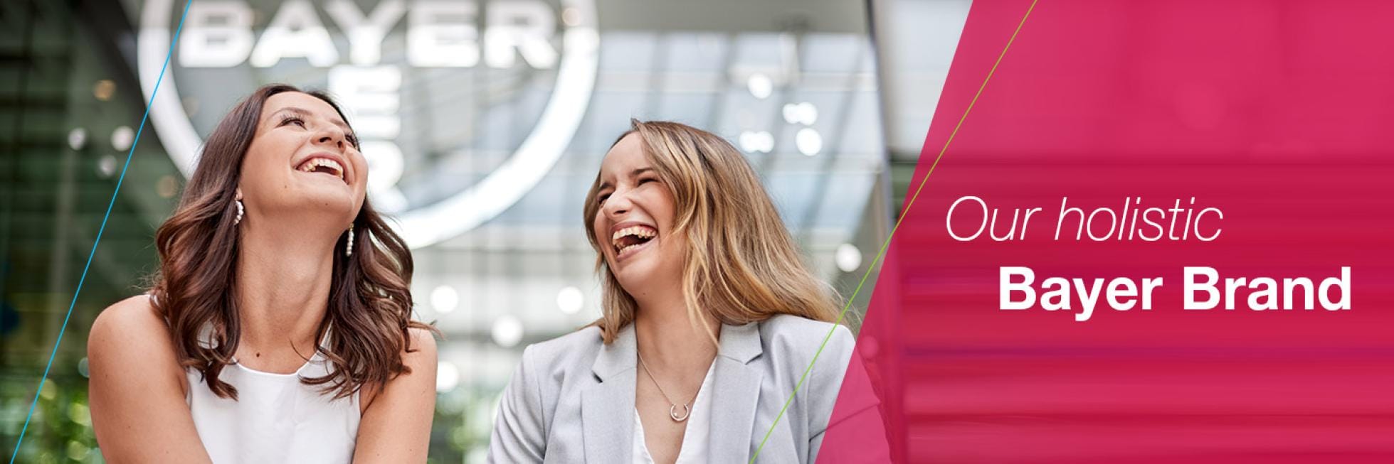 Two smiling women in front of the Bayer Cross and the words: Our holistic – Bayer Brand