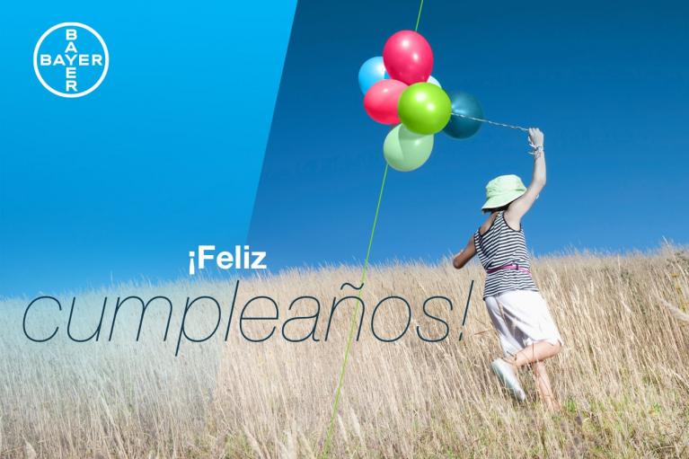 A person in a field holding colorful balloons, with the text "¡Feliz cumpleaños!" and the Bayer logo in the top left corner.