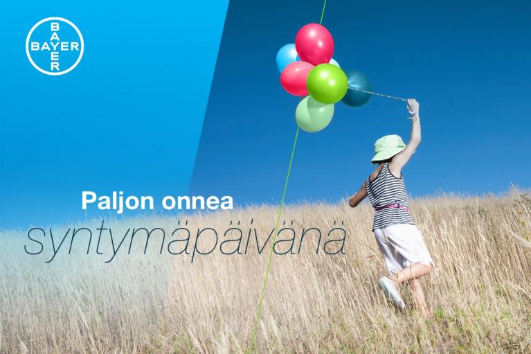 A child runs through a field with colorful balloons against a blue sky. Finnish text reads "Paljon onnea syntymäpäivänä" and a Bayer logo is in the top left corner.