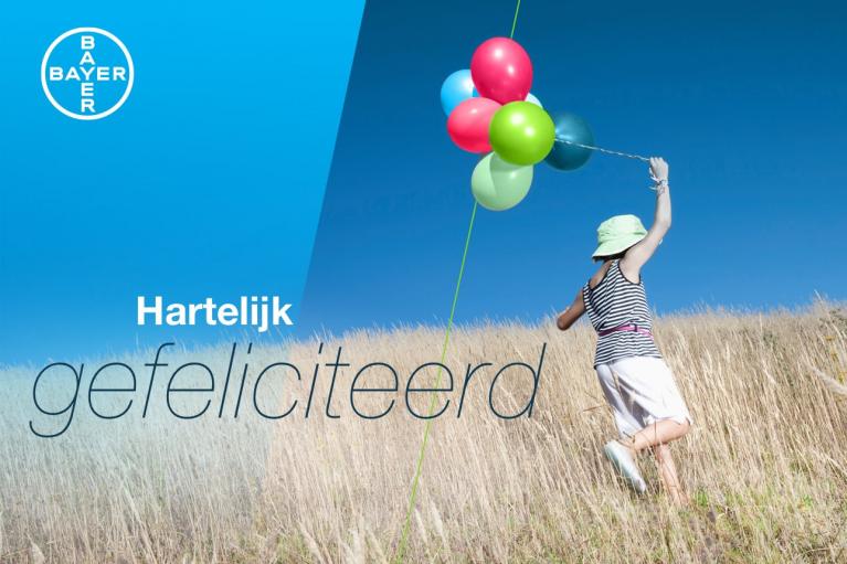 A person holding colorful balloons runs through a grassy field. The text says "Hartelijk gefeliciteerd" with a Bayer logo in the corner.