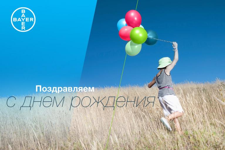 Child holding colorful balloons in a grassy field under a clear sky with "Поздравляем с днем рождения" text and Bayer logo.