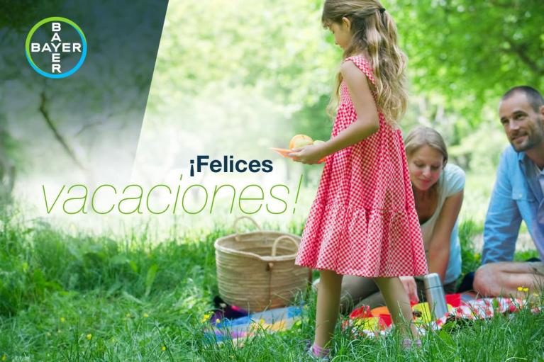 A family enjoys a picnic on grass. A girl in a red dress holds an orange. The text reads "¡Felices vacaciones!" A Bayer logo is visible in the top left corner.