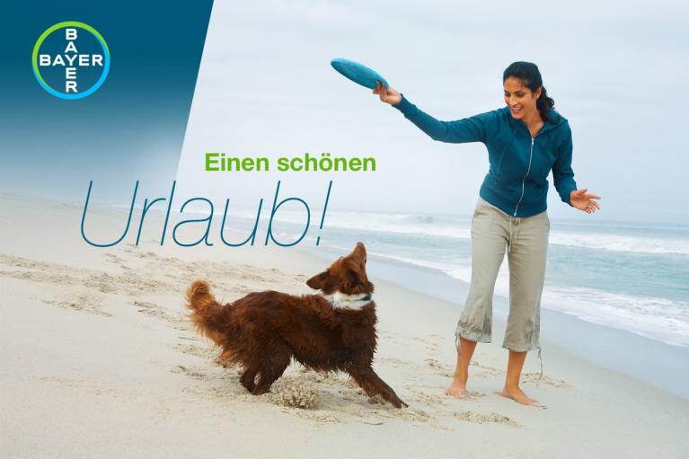 Woman playing fetch with a dog on a beach. Text reads "Einen schönen Urlaub!" in German, with Bayer logo.