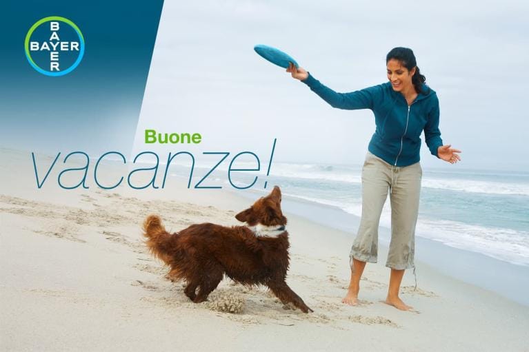 A woman plays fetch with a dog on a sandy beach. The text reads "Buone vacanze!" and there is a Bayer logo.