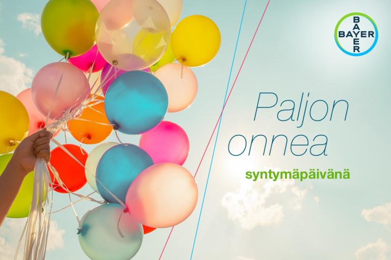 A hand holds brightly colored balloons against a blue sky. Finnish text reads "Paljon onnea syntymäpäivänä," meaning "Happy Birthday." Bayer logo is in the top right corner.