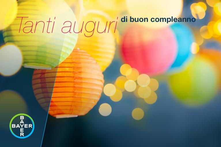 Colorful paper lanterns with warm lights in the background and an Italian birthday greeting. Bayer logo in the corner.