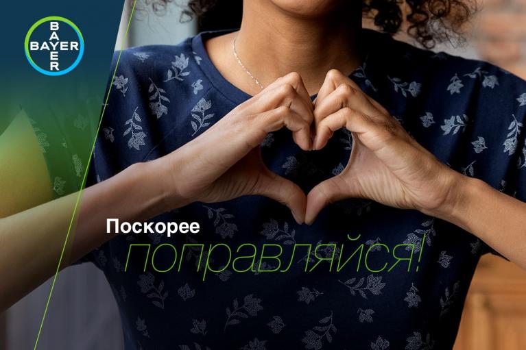 A person forms a heart shape with their hands, wearing a floral shirt. The Bayer logo is in the corner. Text in Russian reads, “Get well soon!”.