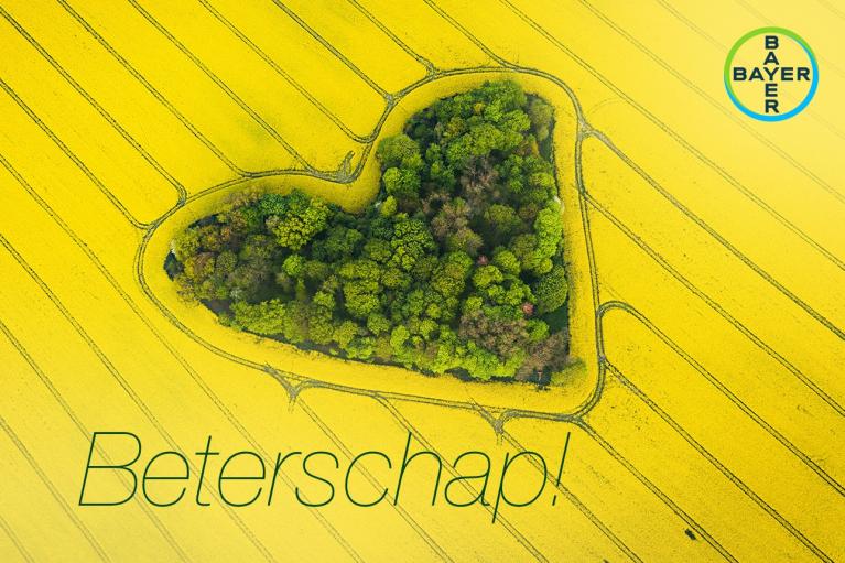 Aerial view of a heart-shaped cluster of trees in a yellow field with the word "Beterschap!" and Bayer logo.