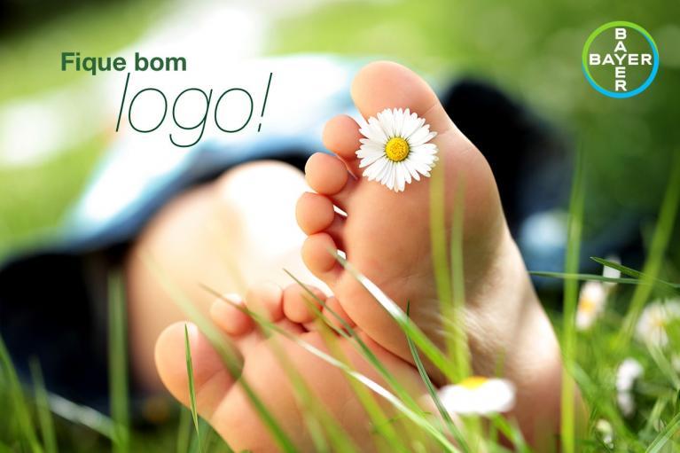 Close-up of a person's foot with a daisy on the toes, resting on grass. The text reads "Fique bom logo!" and shows the Bayer logo in the top right corner.