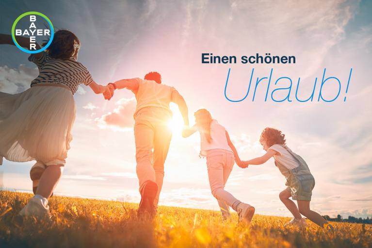 Four people hold hands while running in a sunlit field. The text reads "Einen schönen Urlaub!" with a Bayer logo in the corner.