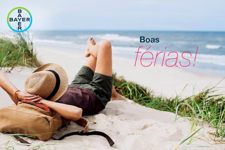Person relaxing on a sandy beach with a hat and a backpack. Text reads "Boas férias!" and the Bayer logo is visible.