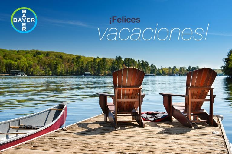 Two wooden chairs on a dock facing a lake with trees in the background. A canoe is nearby. Text reads "¡Felices vacaciones!" A Bayer logo is in the corner.