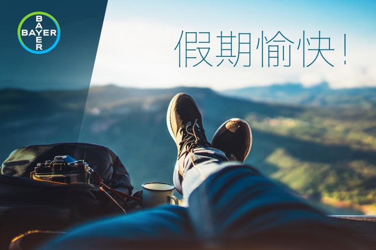 Person relaxing outdoors with legs extended, camera and backpack nearby, overlooking scenic landscape. Bayer logo in the corner. Text in Chinese reads "Happy Holidays!.