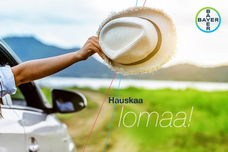 A hand extends from a car window, holding a straw hat. The background features a scenic landscape with hills and a body of water. The text reads "Hauskaa lomaa!" with the Bayer logo in the corner.