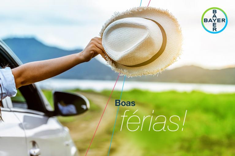A person extends a hand holding a straw hat out of a car window, with "Boas férias!" on the image. A scenic landscape and Bayer logo are visible.