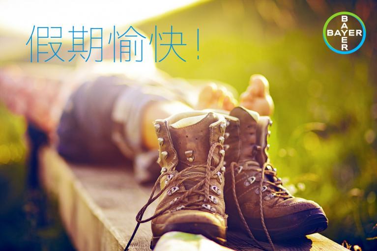 Person relaxing outdoors, lying on a wooden surface with hiking boots off. Chinese text on the image and a Bayer logo in the corner.