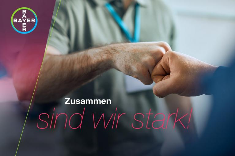 Two people fist-bumping with the Bayer logo in the corner. The text reads, "Zusammen sind wir stark!" in a bold font.