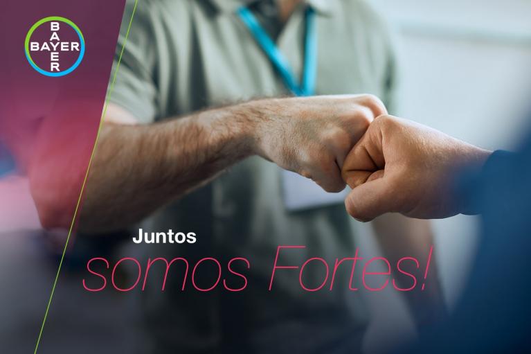 Two people fist-bumping with blurred background. Text: "Juntos somos Fortes!" and Bayer logo in the corner.