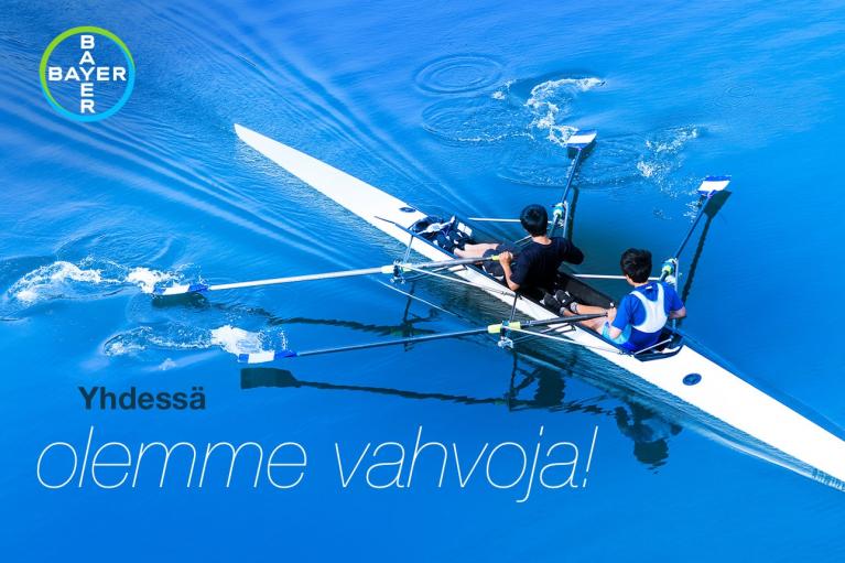 Two people rowing in a blue water rowing shell. Text reads, "Yhdessä olemme vahvoja!" with a Bayer logo in the top left corner.