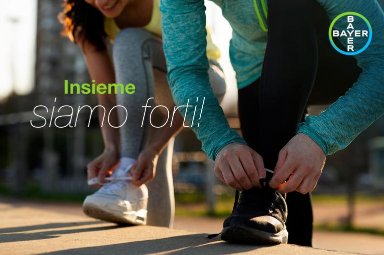 Two people tying their athletic shoes outdoors with the text "Insieme siamo forti!" and a Bayer logo.
