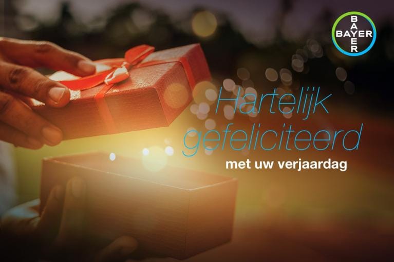 Hands opening a gift box with the text "Hartelijk gefeliciteerd met uw verjaardag" and a Bayer logo in the corner.